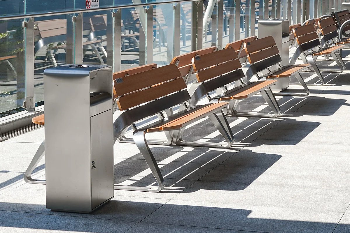 Row of hardwood and stainless steel park benches lined up at even intervals on an urban plaza