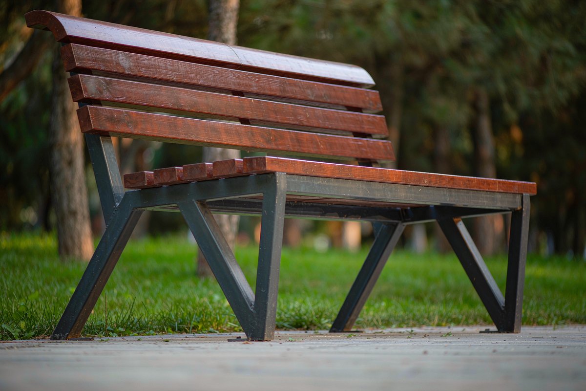 Side view close-up of a wooden park bench on a path showing the seat height above the pavement relative to its steel legs